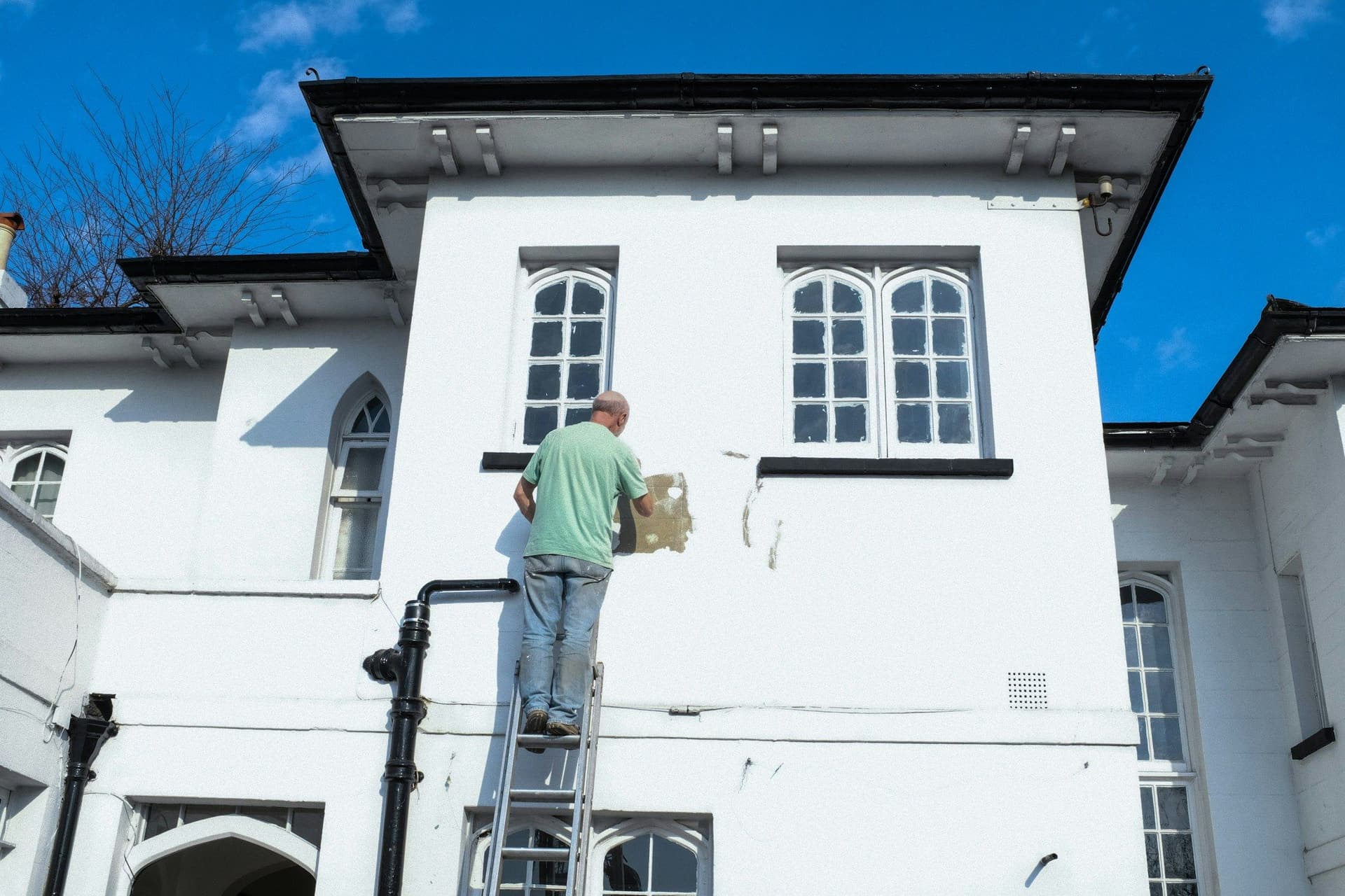 Professional painter on a ladder preparing a white house exterior for repainting